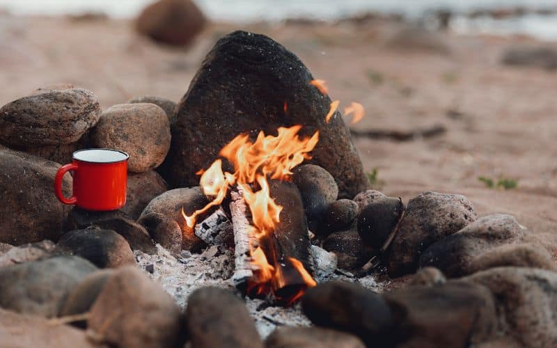 Small campfire in a fire ring with a metal mug beside it