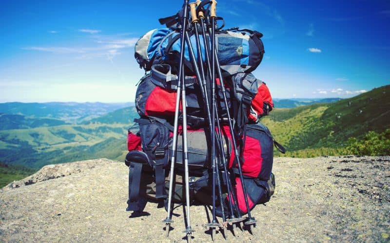 Threee sets of trekking poles leaning against a pile of backpacks