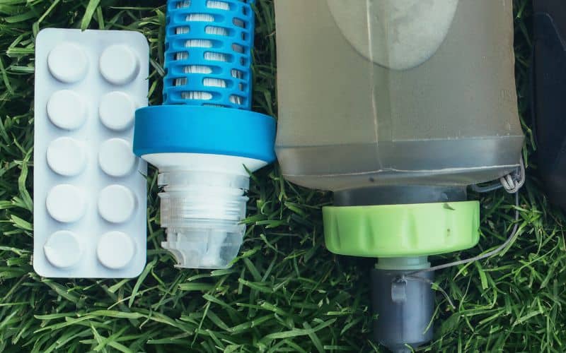 Water purification tablets and filtration device beside a water bottle