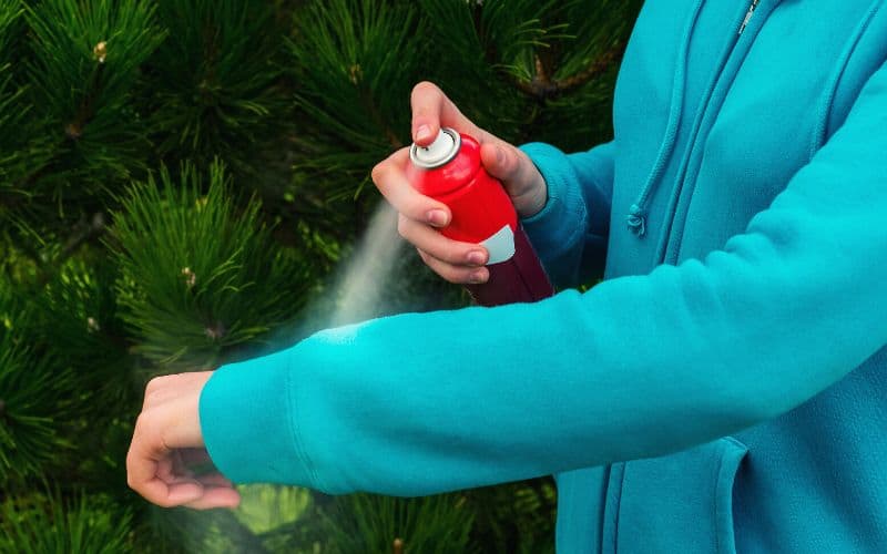 Woman wearing long sleeved top spraying hand with mosquito spray