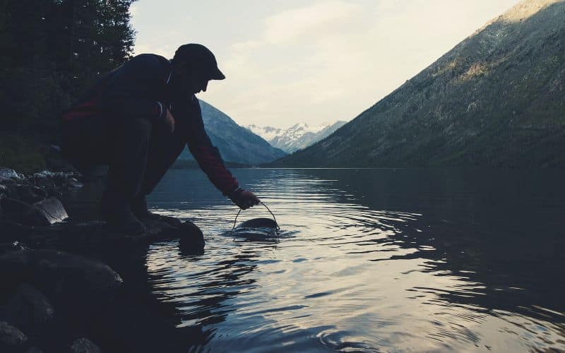 Man taking water from a river surrounded by mountains