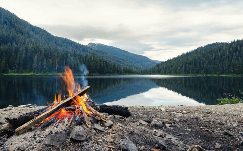 Campfire in front of a lake and mountains