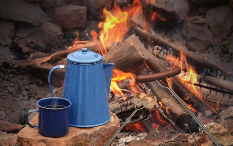 Coffee pot and mug sitting in front of a campfire