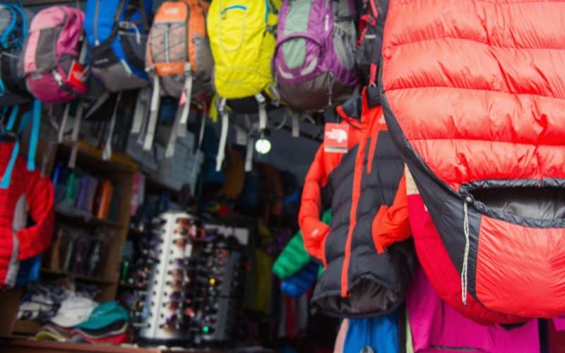 Camping store wall with backpacks lining it and a hung up sleeping bag