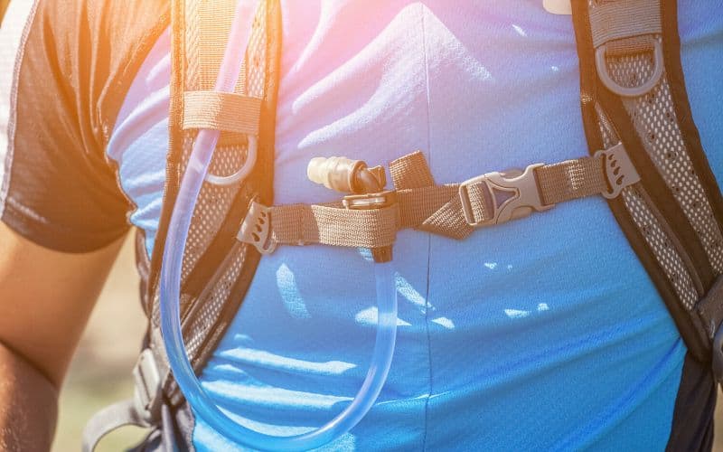 Drinking tube of hydration pack threaded through backpack straps