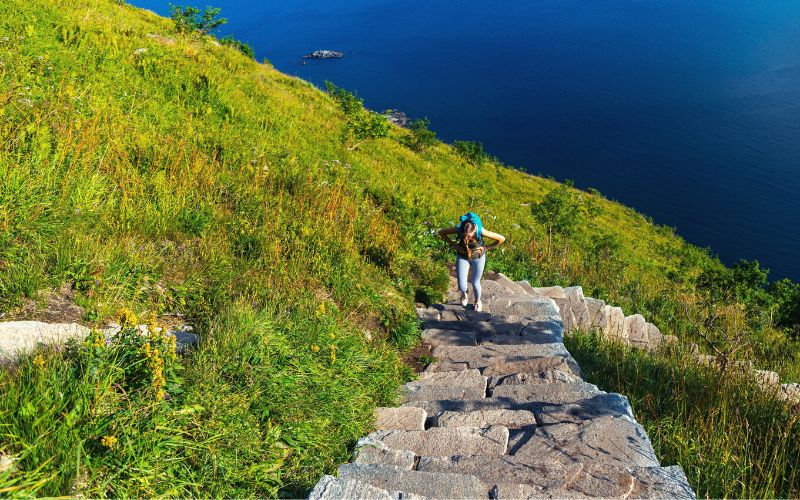 Girl walking up stairs with backpack on with the ocean below her