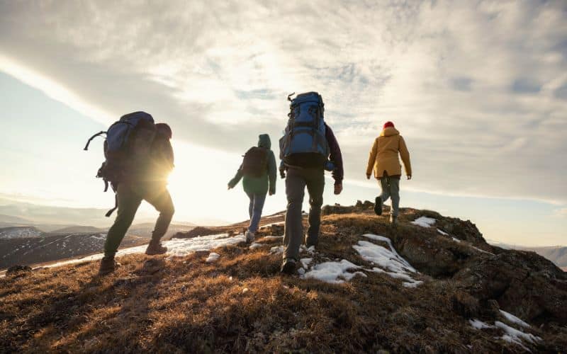 Group of hikers wearing backpacks reaching the summit of a mountain