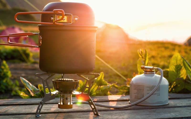 Camp stove and pot attached to a gas canister with sunlight streaming through them