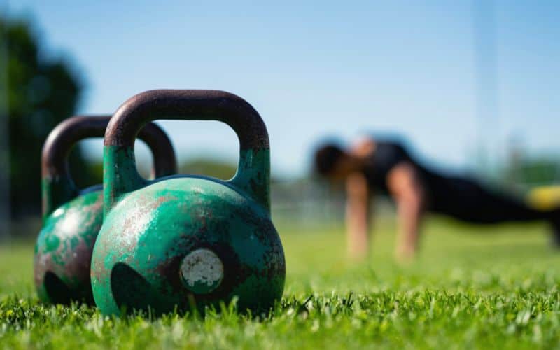 Kettlebells sitting in foreground with a man doing push ups in the distance 