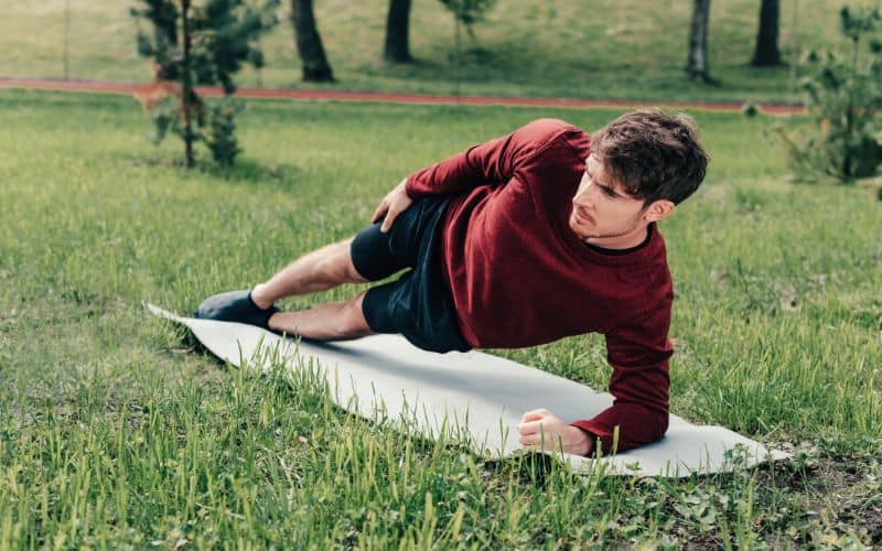 Man doing a side plank on the grass in a park