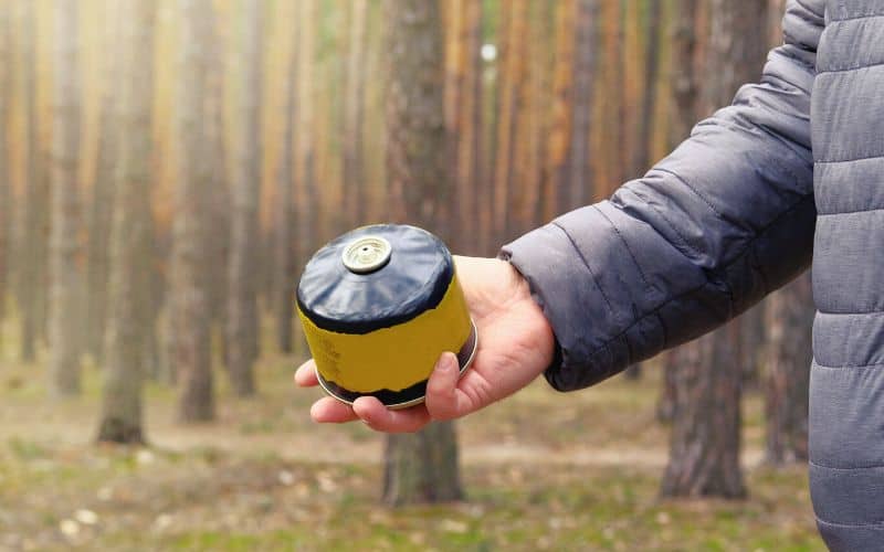 Man holding butane gas canister in front of a forest of trees