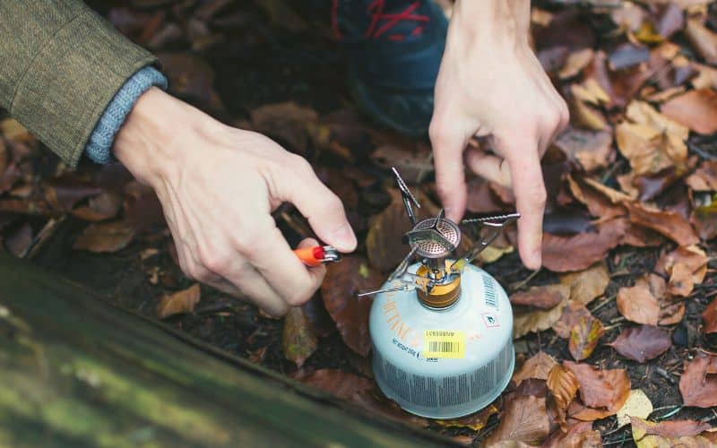 Man lighting a camp stove attached to a gas can