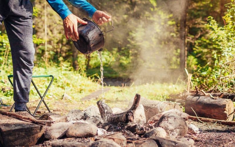 Man pouring water over campfire to extinguish it