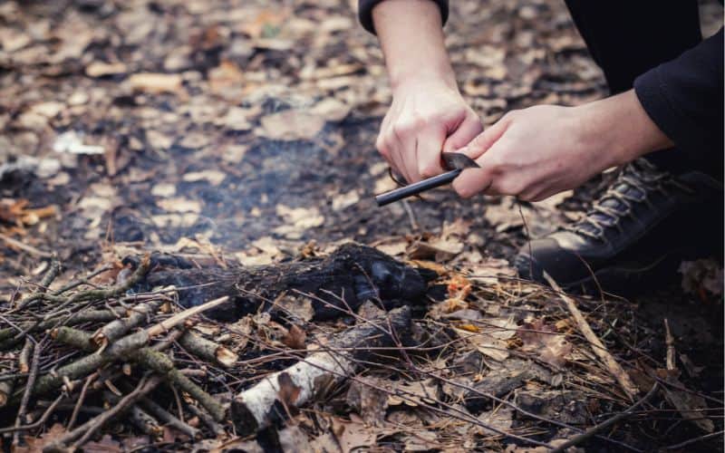 Man using knife on ferro rod to create metal shavings in kindling pile