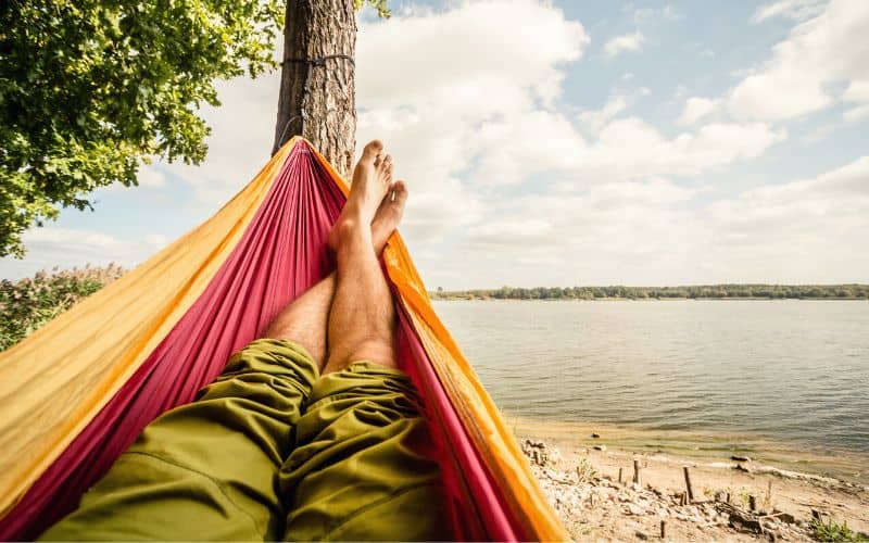 Mans legs sticking out the end of a hammock with a beach view
