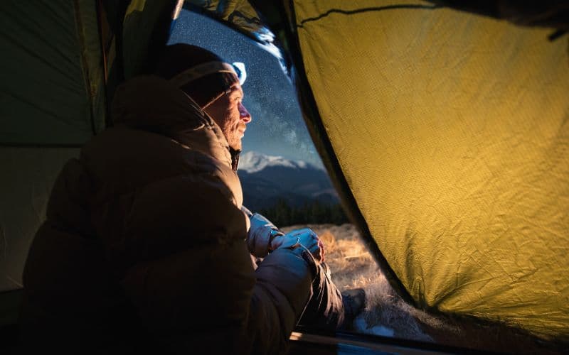 Camper at nighttime wearing headlamp inside of tent
