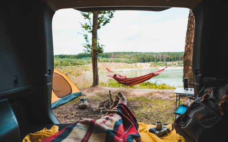 Camper in trunk of car looking out at pitched tent and hammock 