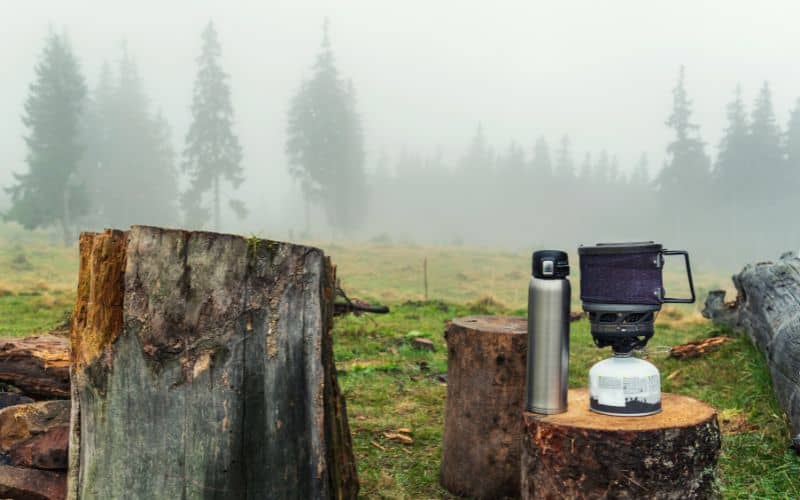 Camping stove, pot and thermos sitting on tree stump