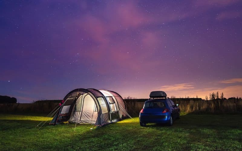 Lit up tent pitched next to parked car after sun has set
