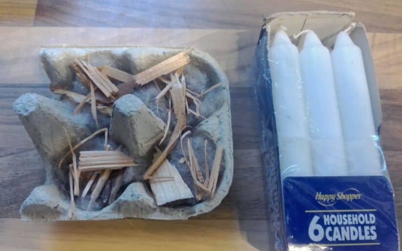 Egg carton filled with lint and wood shavings beside candles
