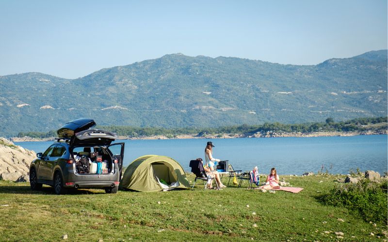 Family beside tent and car camped out at a lakeside