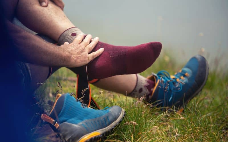 Hiker wearing socks with boots off holding ankle 