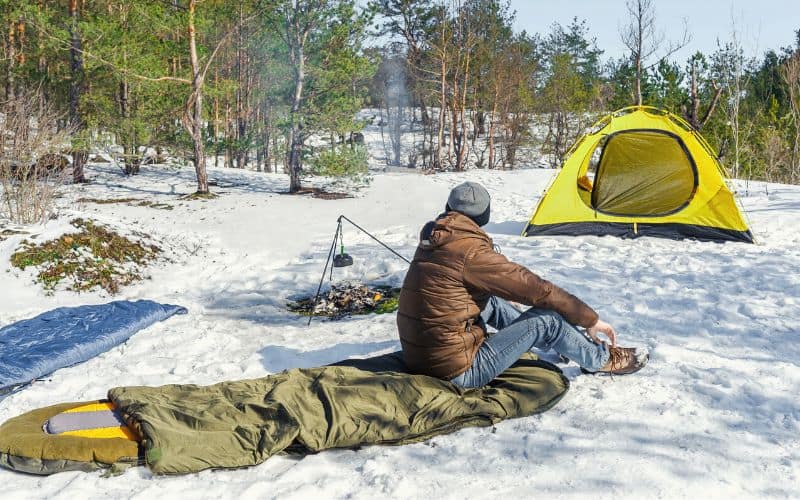 Man sitting on sleeping pad outside tent pitched in the snow