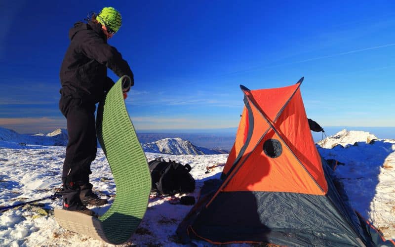 Man unrolling a sleeping mat in front of a tent in the snow