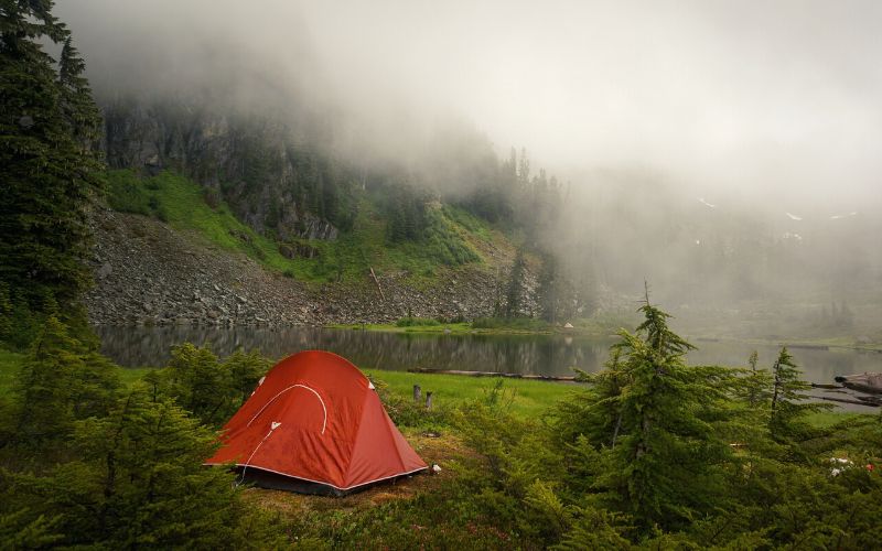 Orange tent in the fog pitched beside an alpine lake