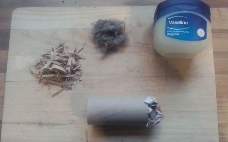 Toilet roll blocked off with scrunched up paper sitting beside lint, wood shavings, and vaseline 