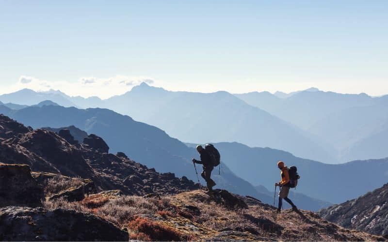 Two hikers with trekking poles climbing a mountain