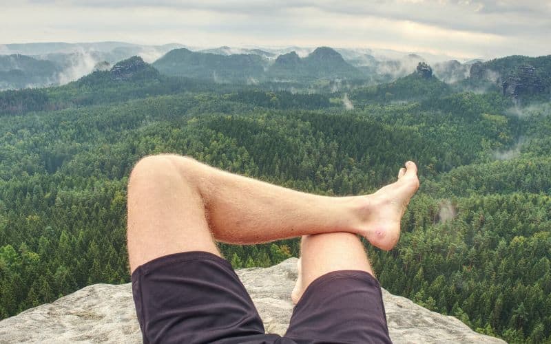 Hiker with a blister resting his legs whilst looking at mountain view over clifftop