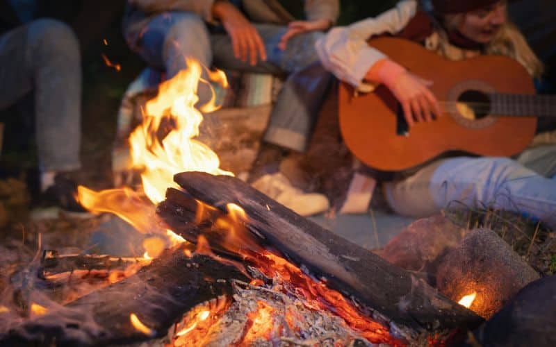 Close up of camper playing guitar behind campfire
