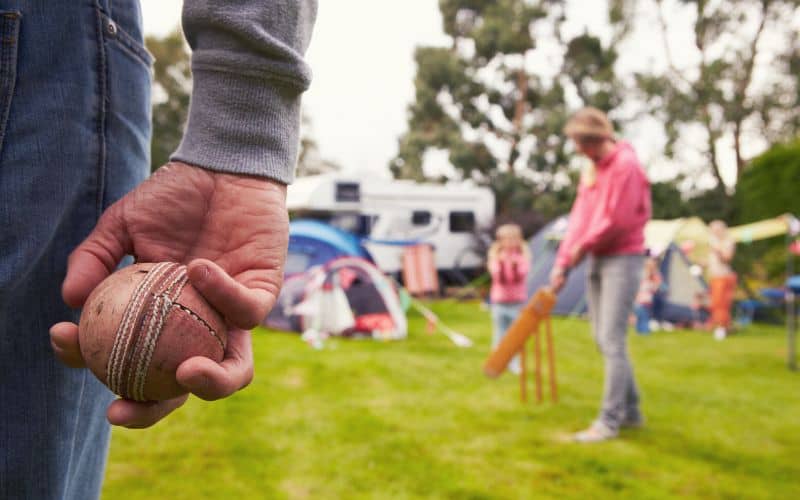 Family playing cricket at campsite with RV in background