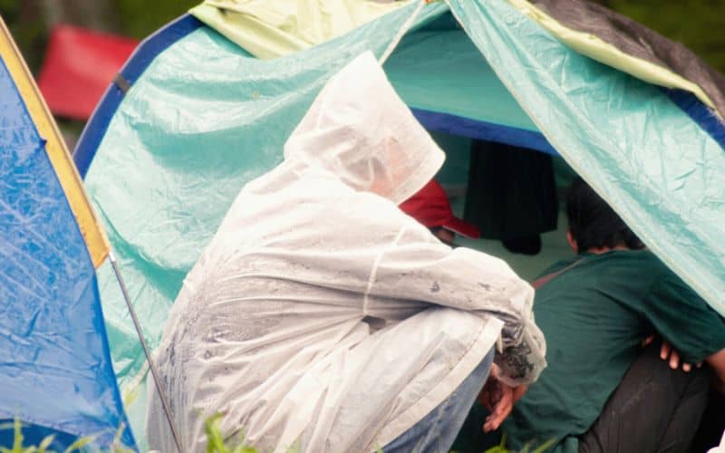 Camper in rain poncho kneeling beside tent opening