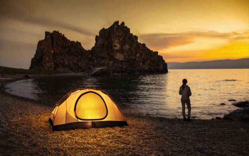 Camper stood outside tent at shoreside watching the sunset