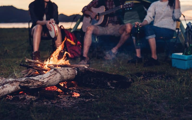 Campers around campfire playing a guitar and tamborine