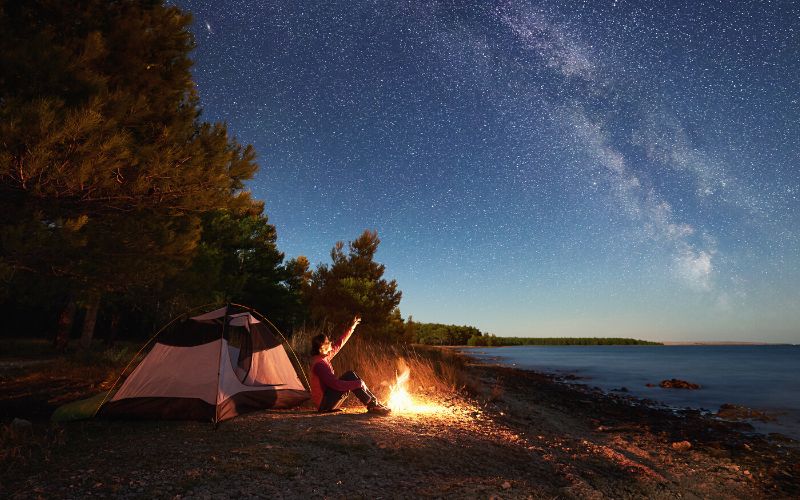 Solo camper beside tent and campfire looking at the night sky