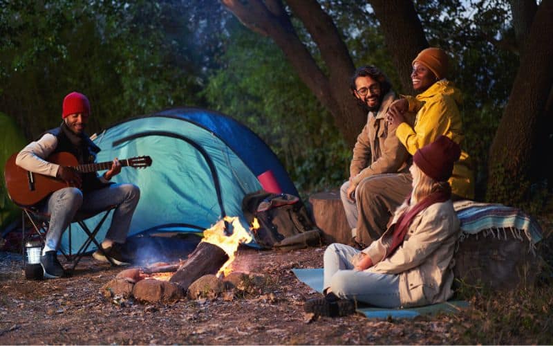 Camping group around campfire with guitar