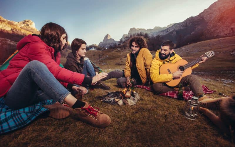 Camping group playing guitar around campfire in the mountains