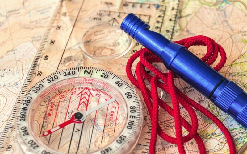 Close up of a compass and rescue whistle lying on top of a map 