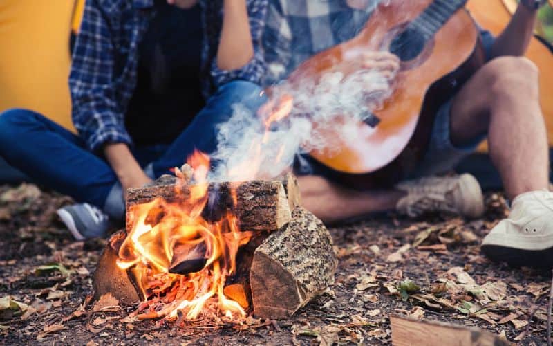 Couple sitting behind campfire with a guitar
