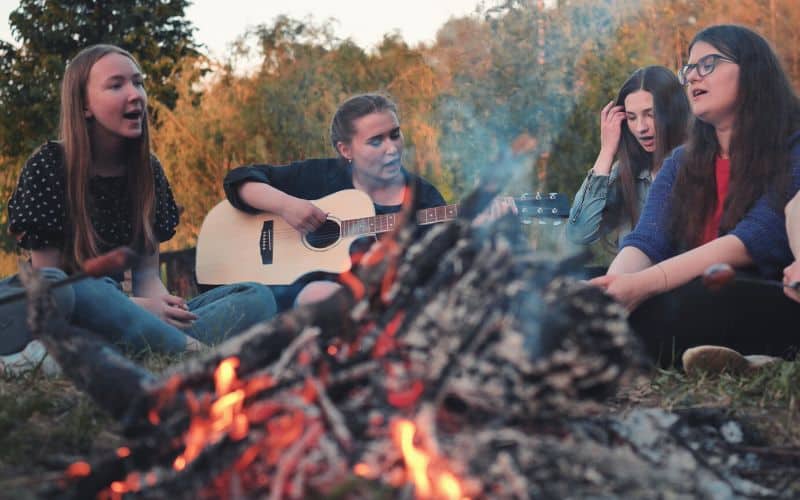 Group of girls singing around campfire to a guitar