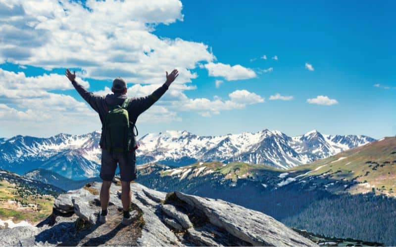 Hiker on top of mountain with hands in the air doing the human Y-shape