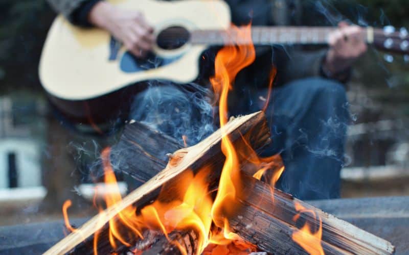 Man playing guitar in front of a campfire