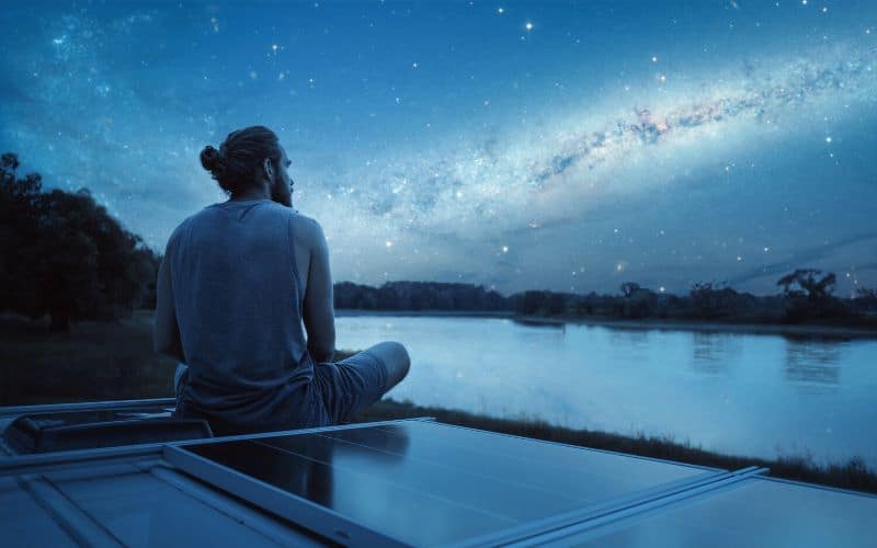 Man sitting on top of campervan watching stars in the night sky