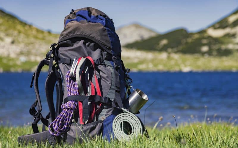 Mountain climbing equipment attached to backpack in front hills and a lake