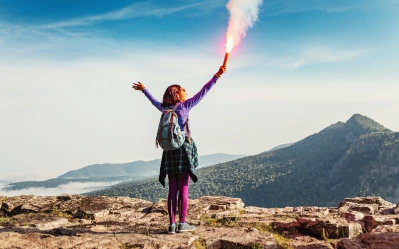 Woman hiker holding a flare in a Y-shape on mountain top