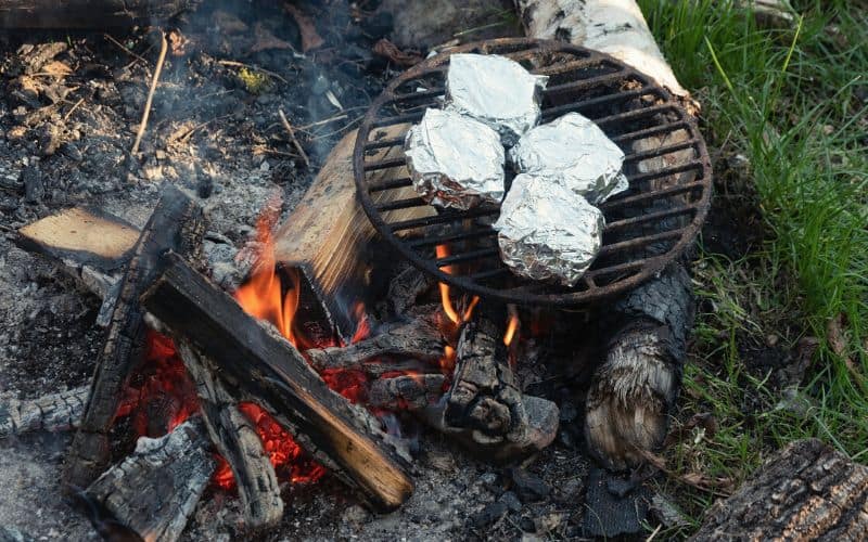 Baked potatoes in foil cooking on a grate over a campfire