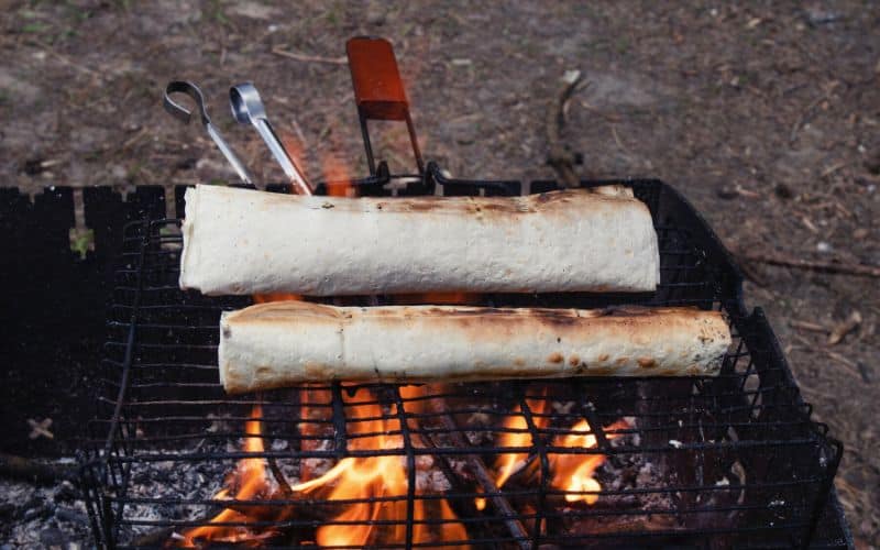 Burritos browning on a grate over a campfire